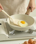 Person holding a silicone turner cooking an egg on a white frying pan with a white kitchen