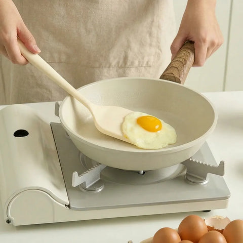 Person holding a silicone turner cooking an egg on a white frying pan with a white kitchen