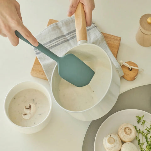Person using a green spatula to serve food from a white bowl on a kitchen counter.