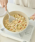 Person stirring fried rice in a pan on a stove with a white background