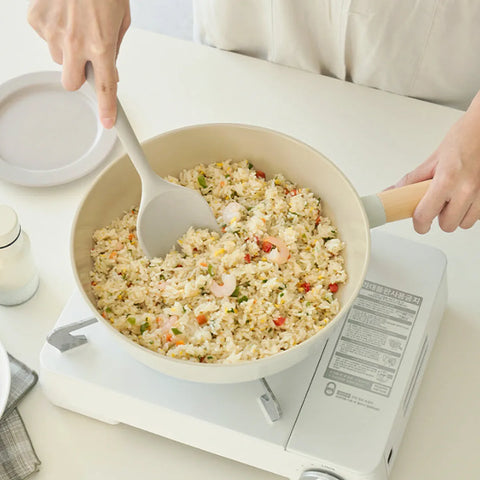 Person stirring fried rice in a pan on a stove with a white background