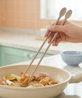 Person using chopsticks to stir food in a pan on a kitchen counter.