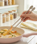 Person using chopsticks to pick up food from a pan on a kitchen counter.