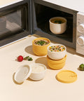 Assorted rice containers stacked on top of each other with an open microwave in the background