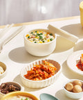Assorted dishes with a bowl of rice, side dishes and utensils on a white table