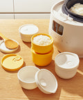 Set of yellow and white rice containers with a rice cooker in the background.