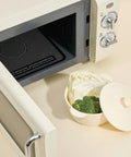 Vintage-style microwave oven with a bowl of vegetables on a kitchen counter.