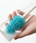 Hand holding a glass with a blue cleaning brush inside, against a white background