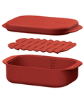 Red silicone steamer dish with lid and rack on a white background