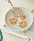 Person cooking shrimp cakes in a frying pan on a small stove.