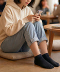Woman on her phone sitting on the floor wearing black ankle socks