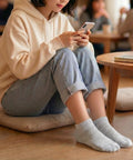 Woman sitting on the floor holding a cell phone wearing gray ankle songs