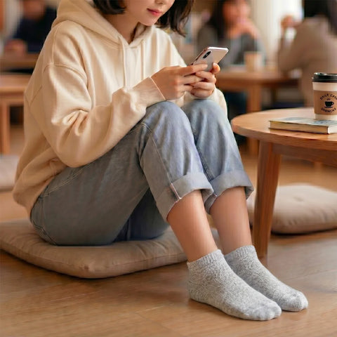 Woman sitting on the floor holding a cell phone wearing gray ankle songs