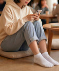 Person sitting on the floor using a smartphone in a casual setting wearing white ankle socks
