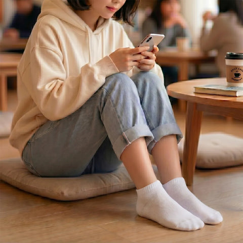 Person sitting on the floor using a smartphone in a casual setting wearing white ankle socks