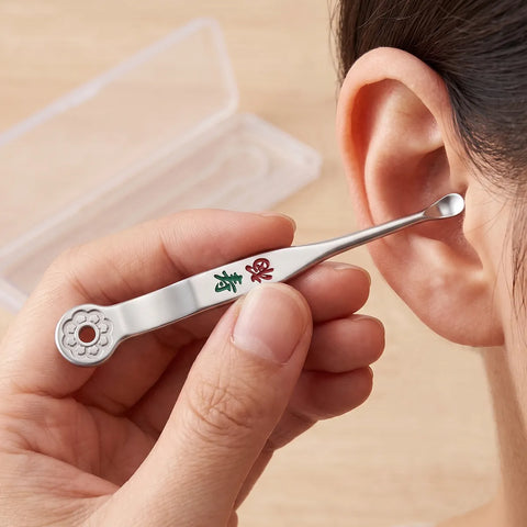 Person using a silver ear cleaning tool to clean their ear with a beige background