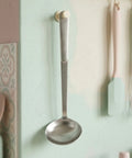 Stainless steel ladle hanging on a white hook in a pastel green and pink kitchen.