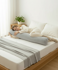 Person sleeping on a bed with a long cylindrical pillow