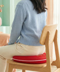 Person sitting on a chair with a red cushion, wearing a blue sweater and beige pants.