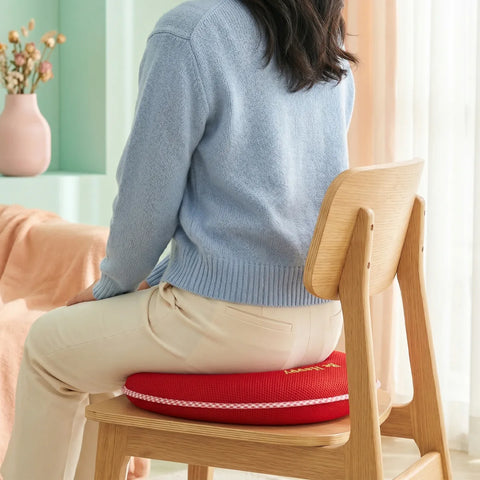 Person sitting on a chair with a red cushion, wearing a blue sweater and beige pants.
