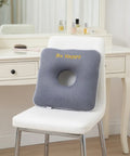 Gray donut cushion with 'Be Happy' text on a white chair in a room setting.