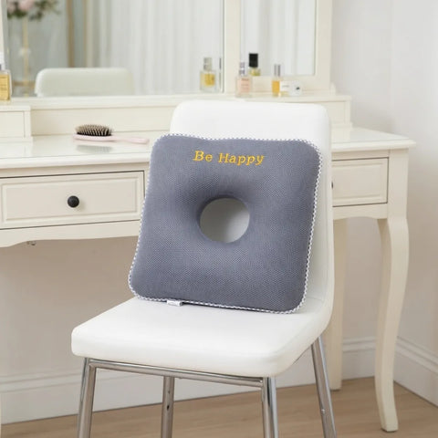 Gray donut cushion with 'Be Happy' text on a white chair in a room setting.