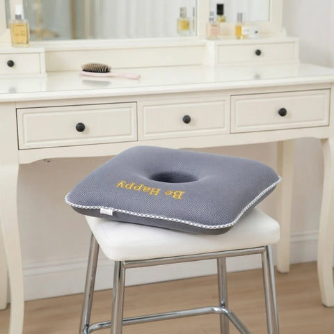 Gray donut pillow with 'Be Happy' text on a white chair in front of a vanity table.