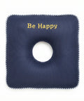 Square navy blue cushion with a circular hole and 'Be Happy' text on a white background