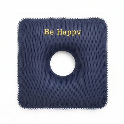 Square navy blue cushion with a circular hole and 'Be Happy' text on a white background