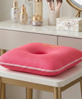 Pink square donut cushion with 'Be Happy' text on a white surface, surrounded by vanity items.