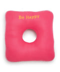 Pink square donut cushion with a circular hole and 'Be Happy' text on a white background