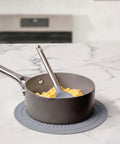 Gray saucepan with a spatula on top of gray silicone mat on a marble countertop 