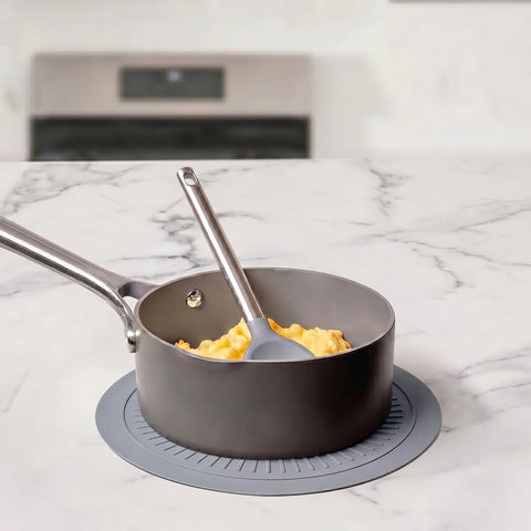 Gray saucepan with a spatula on top of gray silicone mat on a marble countertop 