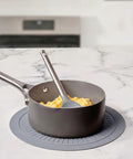 Gray frying pan on top of a gray trivet with a spatula on a marble countertop