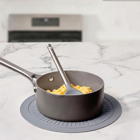 Gray frying pan on top of a gray trivet with a spatula on a marble countertop
