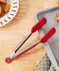 Red tongs on a wooden surface with a tray of bread slices.