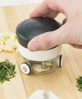 Hand using a garlic press on a wooden cutting board with chopped garlic and herbs.