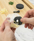 Person using a garlic chopper on a wooden cutting board with minced garlic and herbs.