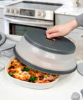 Person placing a gray and clear microwave food cover on a dish of food on a kitchen counter.