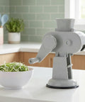 Manual vegetable spiralizer on a kitchen counter with a bowl of spiralized vegetables.