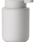 A minimalist matte white cylindrical dispenser with a matching lid and integrated pump, shown on a clean white background with a soft reflection.