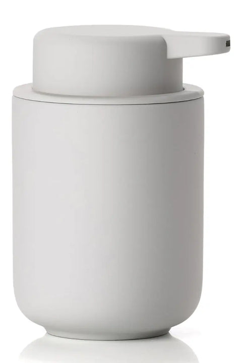 A minimalist matte white cylindrical dispenser with a matching lid and integrated pump, shown on a clean white background with a soft reflection.