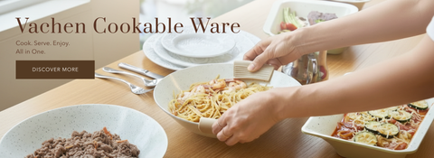 A person serving pasta from a ceramic bowl on a wooden dining table, with other cookware and food dishes visible. Large overlaid text reads 'Vachen Cookable Ware' with a 'DISCOVER MORE' button.