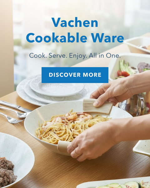 A person's hands use a bamboo utensil to serve spaghetti from a white ceramic bowl on a wooden dining table. The scene is branded with 'Vachen Cookable Ware' text on the left, showing other cookware and prepared food in the background.