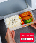 A clear plastic bento container filled with white rice, broccoli, and fried chicken, being pulled out of a white microwave by two hands. A red text box at the bottom right highlights heat resistance up to 140°C.