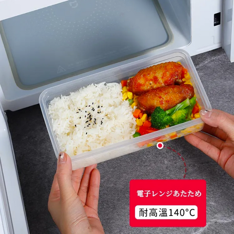 A clear plastic bento container filled with white rice, broccoli, and fried chicken, being pulled out of a white microwave by two hands. A red text box at the bottom right highlights heat resistance up to 140°C.