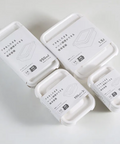Four white plastic storage containers with lids, each wrapped in a white paper sleeve with Japanese text and size markings (950ml, 1.5L, 550ml 2-piece, 300ml 2-piece), arranged on a light gray background.