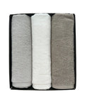 Three folded towels in gray, white, and beige in a black box on a white background