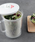 Salad spinner with fresh greens on a gray surface, next to a bowl of salad.