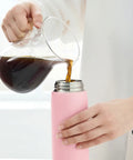 Person pouring coffee from a glass carafe into a pink thermos.